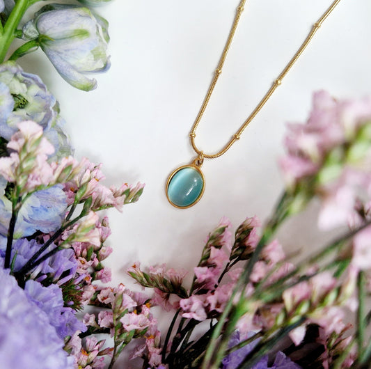 close up of gold aquamarine necklace. Surrounded by flowers.