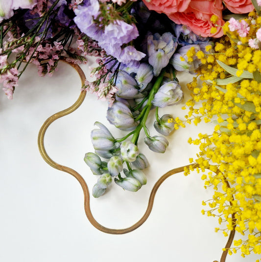 a gold snake chain necklace surrounded by flowers