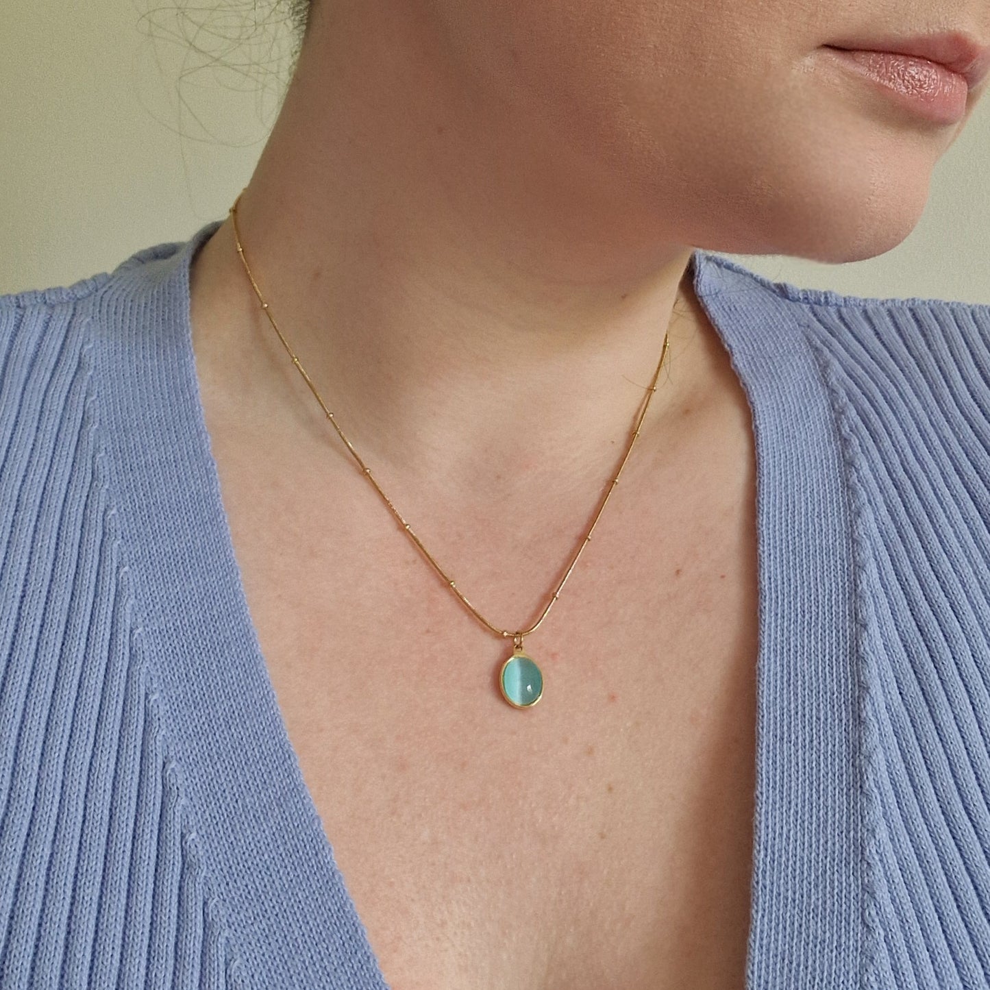 woman wearing gold beaded necklace with an oval aquamarine pendant.
