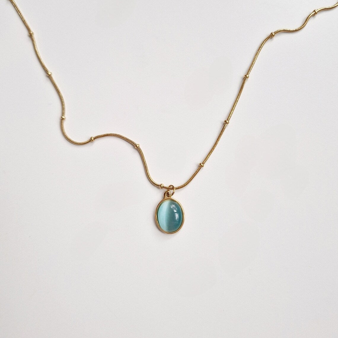 a gold beaded necklace with an aquamarine circle pendant