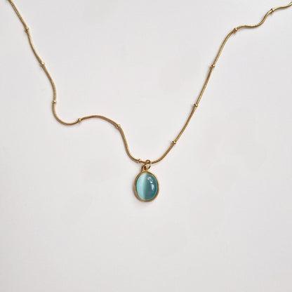 a gold beaded necklace with an aquamarine circle pendant